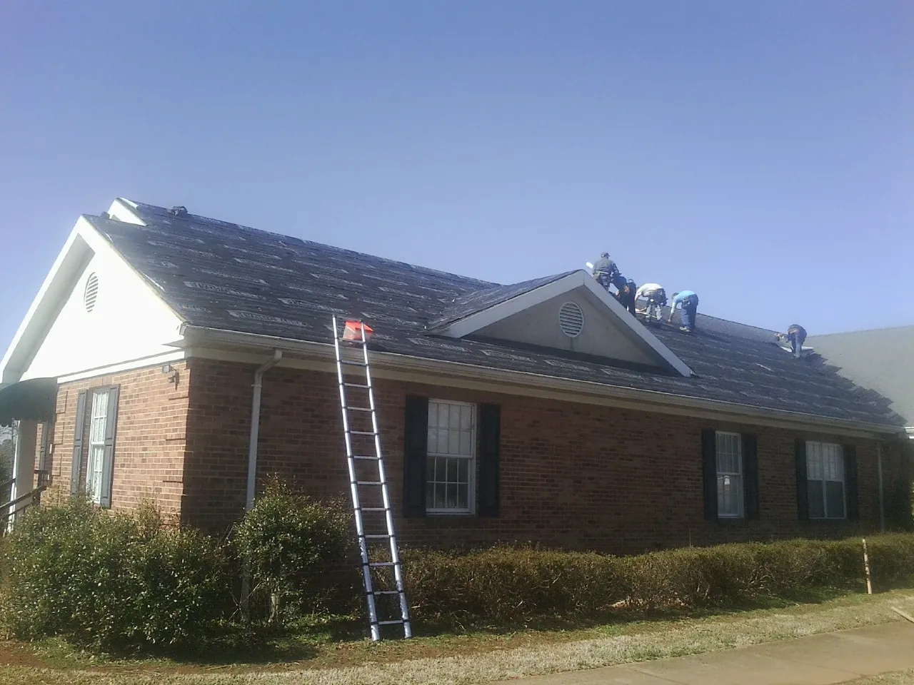 Crew tearing shingles off a brick ranch roof with a ladder set — Metal Roof Repair work by our crew in Irrigon