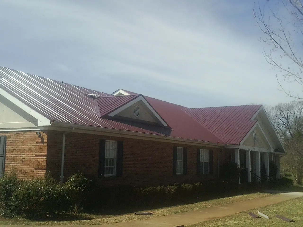 Red metal roof with gabled entries on a long brick building, from a Hail Damage Roof Repair job in Irrigon