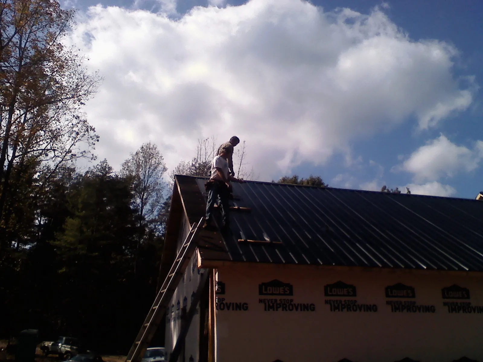 Roofer fastening dark metal panels high against a cloudy sky, from a Roof Inspection job in Irrigon